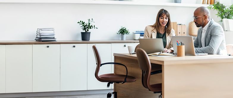 Payments professionals collaborate on laptops in an office.