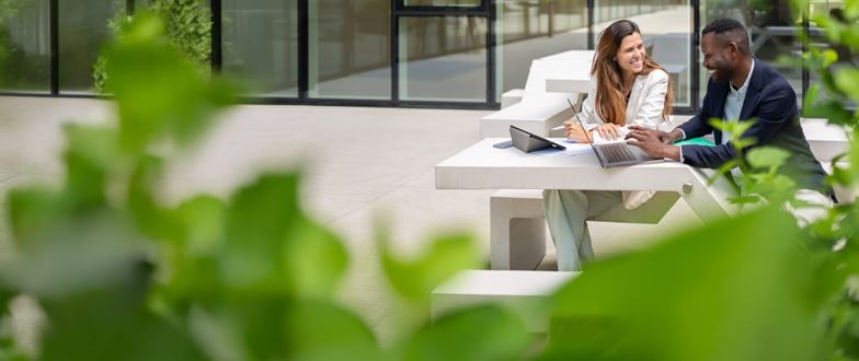Two professionals review data on a laptop outdoors, representing fintech collaboration and progress despite market volatility.
