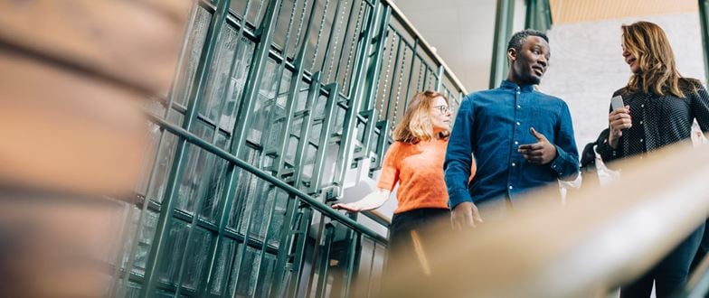 Professionals walk and talk in an office stairwell, representing collaboration in professional and technical services.