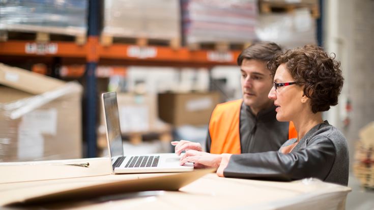 Coworkers looking at a laptop to review inventory problems encountered during a manufacturing external audit.