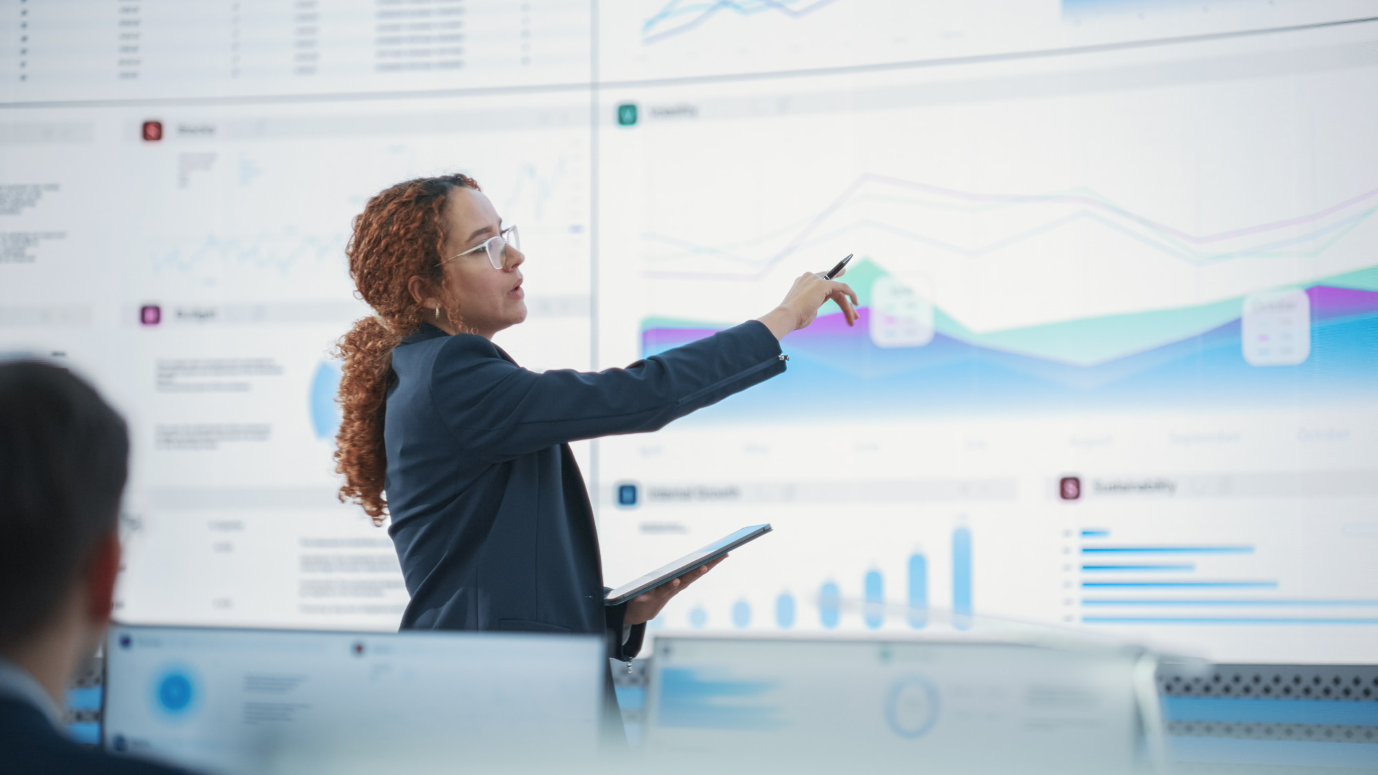 Hispanic senior data scientist analyzes credit risk reports on a large screen while the audit committee explores strategies for mitigating risk in financial services