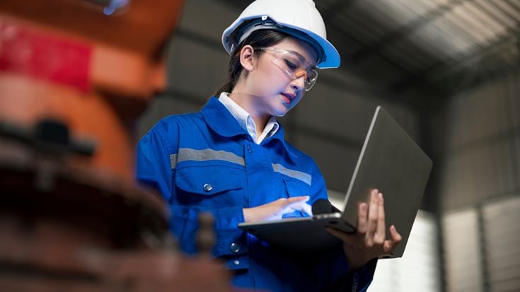 A worker wearing a hard hat and holding a laptop, signifying the digital transformation happening in the manufacturing industry. 