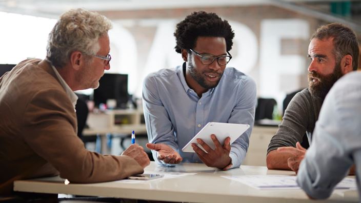 Three professionals seated at a table, analyzing information on a tablet, reflecting the rise in M&A activity in finance.