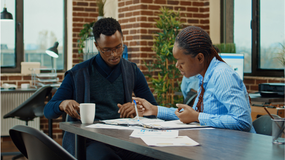 Two individuals engaged in discussion at a table, surrounded by papers and coffee, reflecting on appraisal bias dialogue.