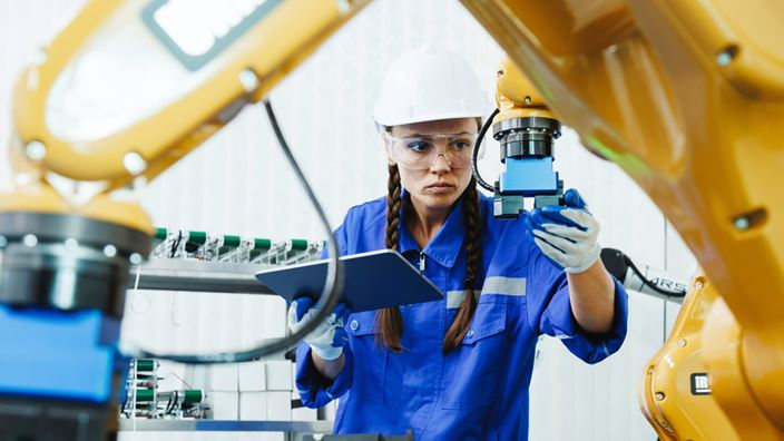 Engineer inspecting a robotic arm on a factory floor, representing manufacturing efficiency and process improvement.