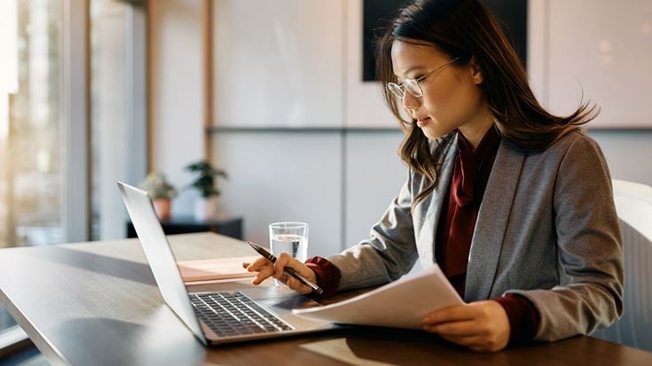 Professional reviews documents and data on a laptop, representing AI-supported decision-making in the public sector.