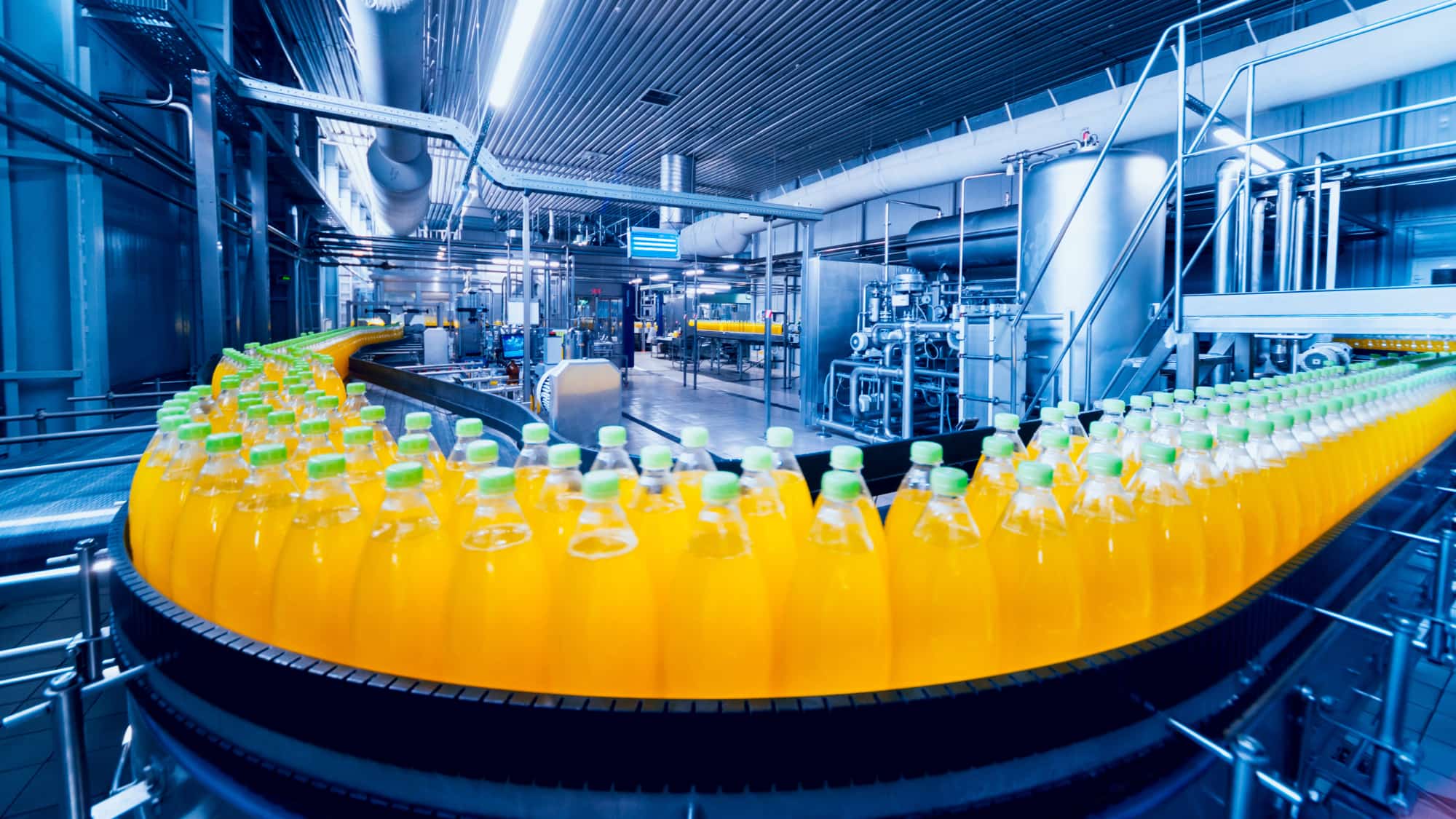 Bottles of orange juice moving along a conveyor belt in a factory setting, showcasing the production process.