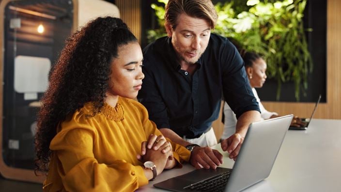 Two professionals review a laptop together, representing shared accountability in enterprise AI risk governance.