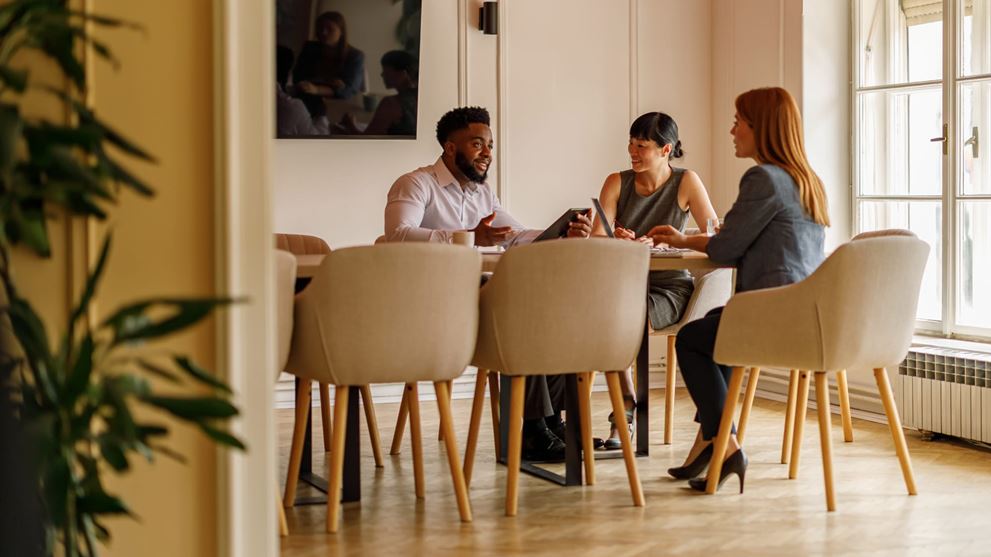 Team meets around a table, representing collaboration and sharing updates in a quarterly HITRUST cybersecurity newsletter.