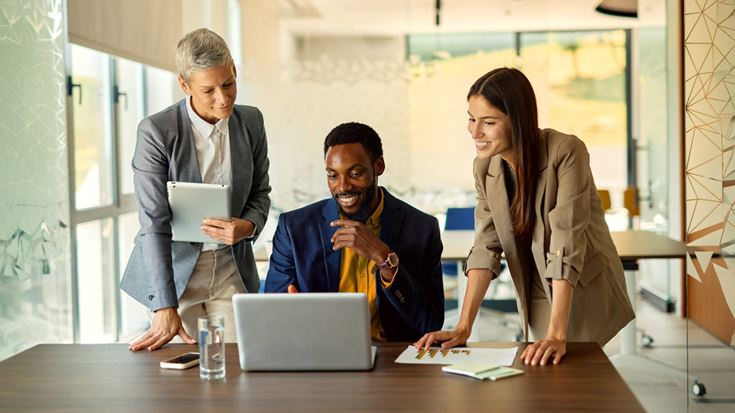 Three business professionals reviewing data on a laptop and tablet, representing collaboration, strategic planning, and business decision-making.