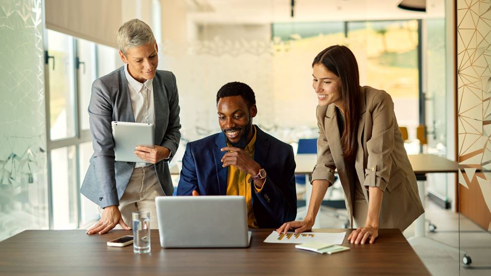Three business professionals reviewing data on a laptop and tablet, representing collaboration, strategic planning, and business decision-making.