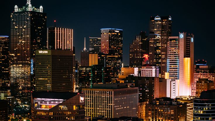 Downtown Dallas skyline illuminated at night, featuring office towers and the city’s business district.