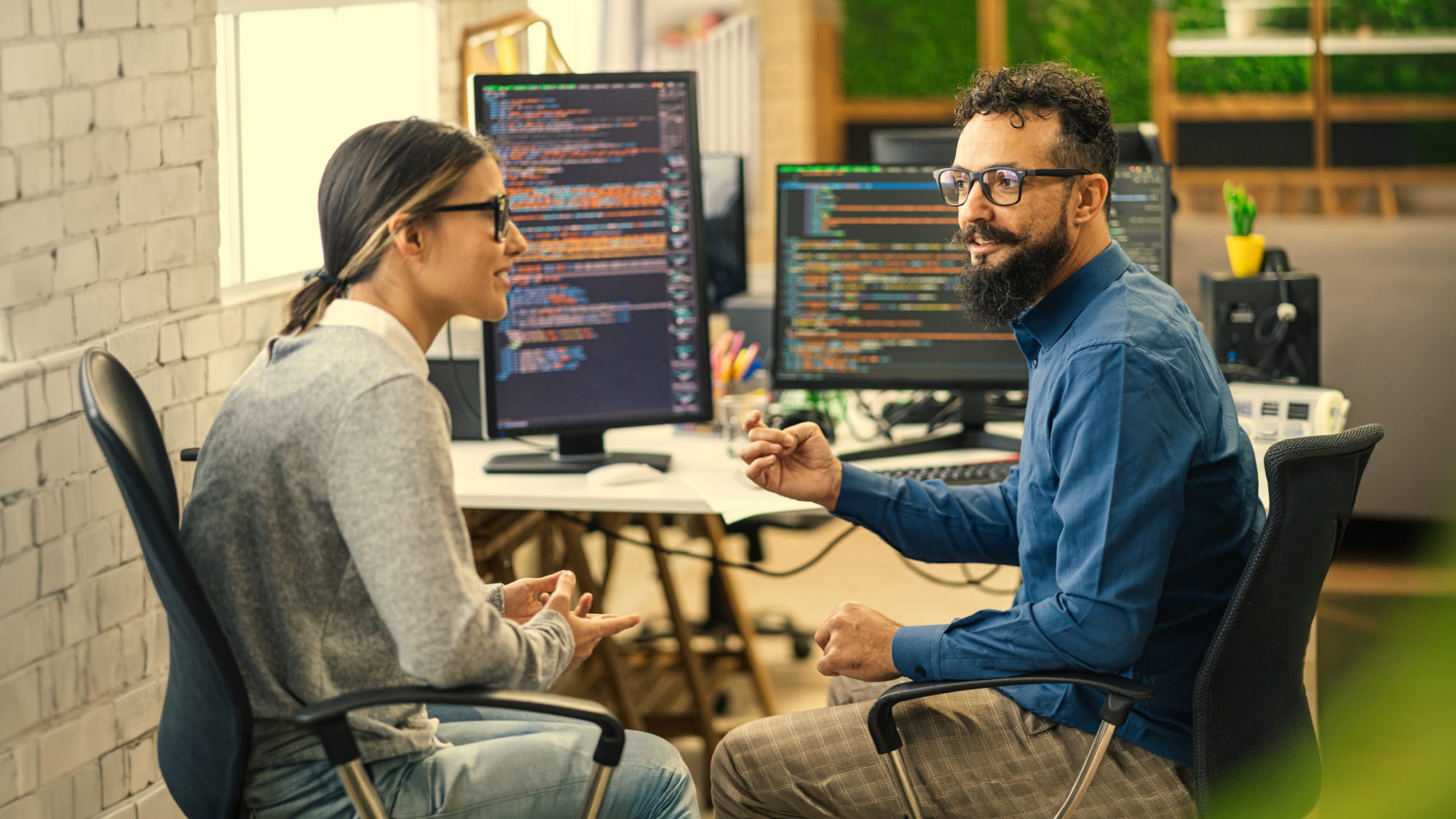 Two professionals discuss software code in an office, symbolizing collaboration on internal-use software updates under ASU 2025-06.