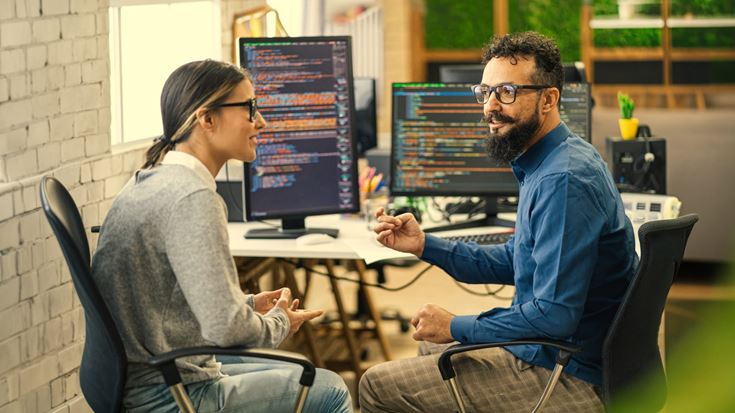 Two professionals discuss software code in an office, symbolizing collaboration on internal-use software updates under ASU 2025-06.
