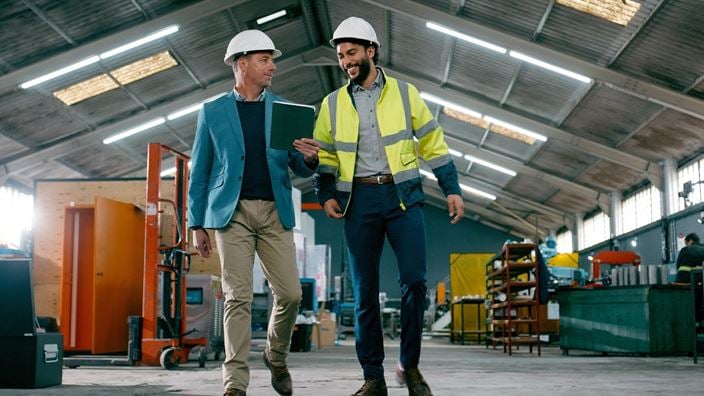 Manufacturing professionals reviewing a tablet while walking through a production facility, discussing operations and working capital.