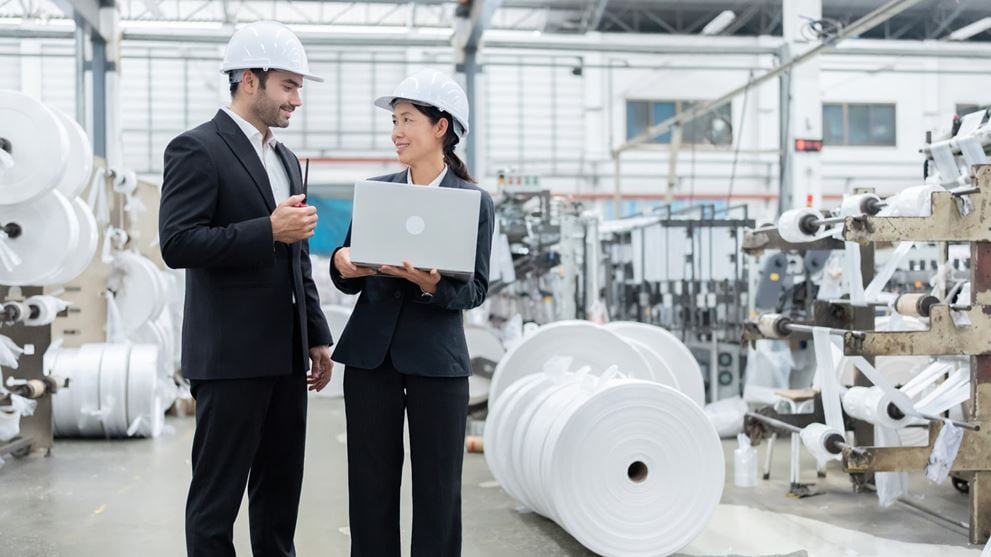 Manufacturing professionals reviewing production data on a laptop in a plastics manufacturing facility.