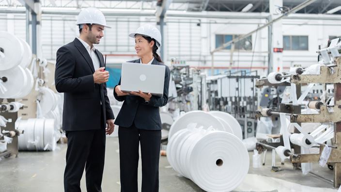 Manufacturing professionals reviewing production data on a laptop in a plastics manufacturing facility.
