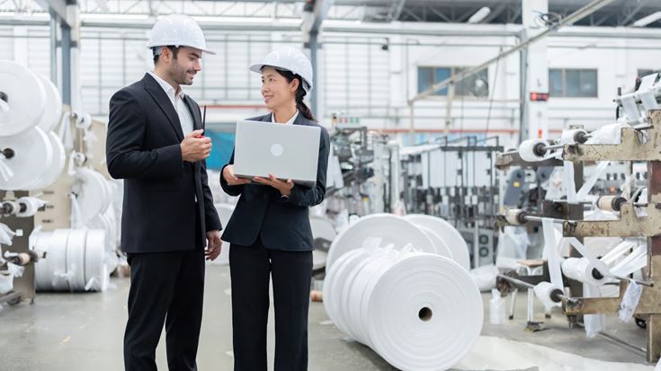 Manufacturing professionals reviewing production data on a laptop in a plastics manufacturing facility.