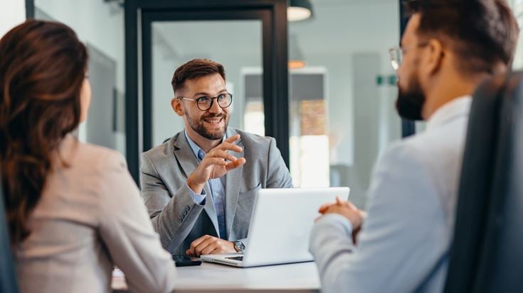 Three business professionals discuss information around a laptop, illustrating collaboration and accountability in banking partnerships.
