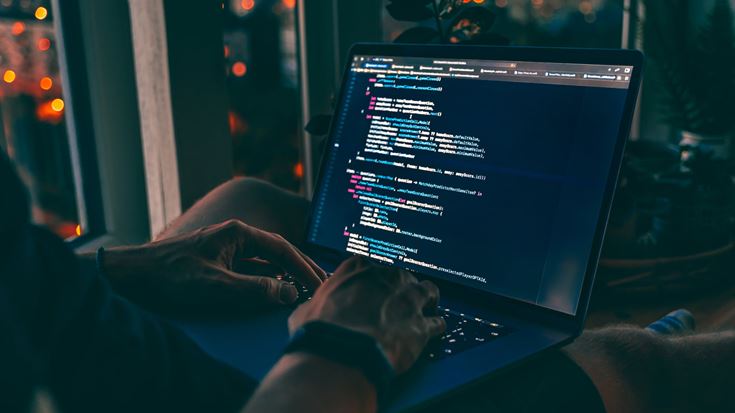 A person sitting on a couch, focused on a laptop during a webinar about the dark web and financial crime risks.