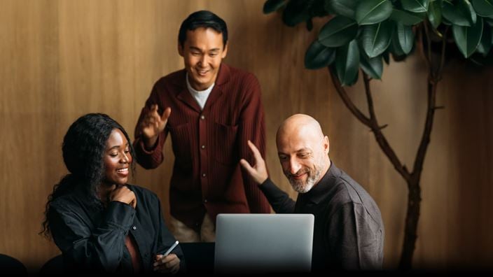 Colleagues smiling around laptop, representing shared learning on Q3 2025 accounting and reporting updates.