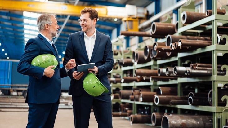 Two professionals discuss materials operations while reviewing information on a tablet in an industrial facility.