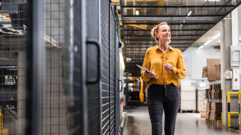 Manufacturing professional using a tablet while walking through a production facility, representing operational performance improvement.