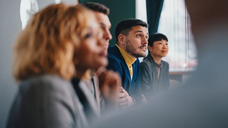 Professionals listen attentively during a meeting, representing peer exchange on finance and risk in the credit union sector.