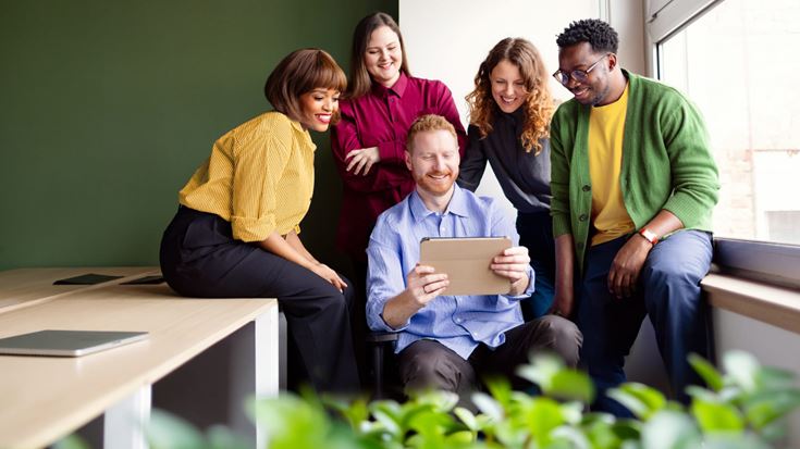 A diverse group of professionals reviews content on a tablet together during a collaborative office meeting.