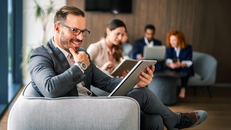 Business professional using a tablet while collaborating with colleagues in a modern office, supporting digital transformation and customer relationship management (CRM) initiatives.