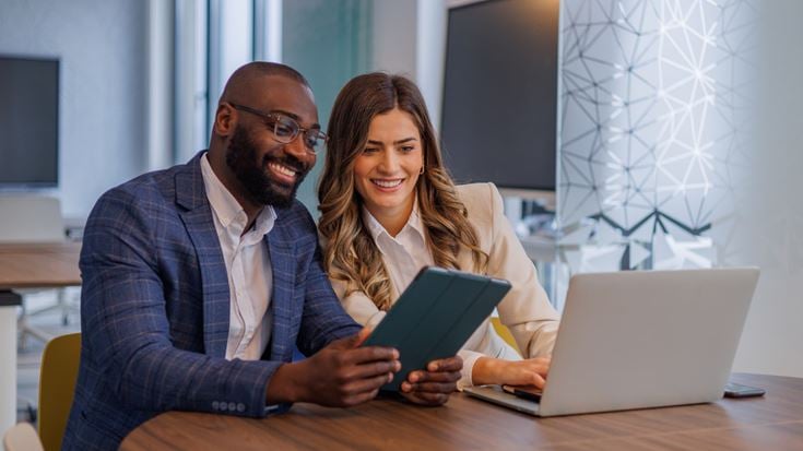 Two business professionals using a tablet and laptop to collaborate on fintech solutions and digital financial technology.