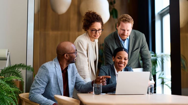 Business professionals collaborating around a laptop during a team meeting, discussing strategy, technology, and business solutions.