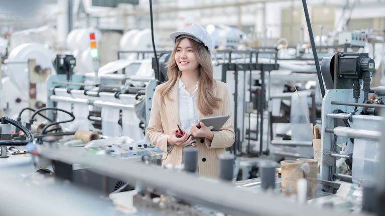 Manufacturing professional using a tablet while assessing automated production equipment