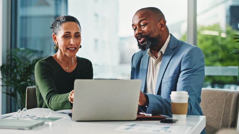 Two business professionals collaborating on a laptop during a meeting, discussing data privacy, compliance, cybersecurity, and business strategy.
