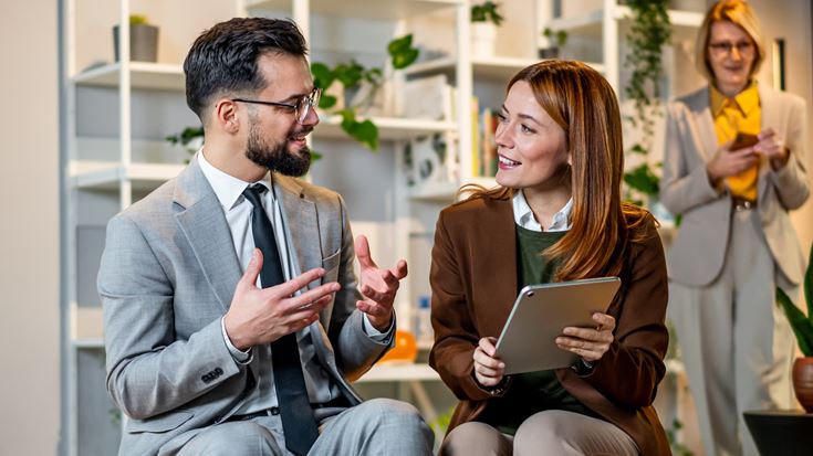 Two business professionals review information on a tablet while discussing digital asset compliance in an office.
