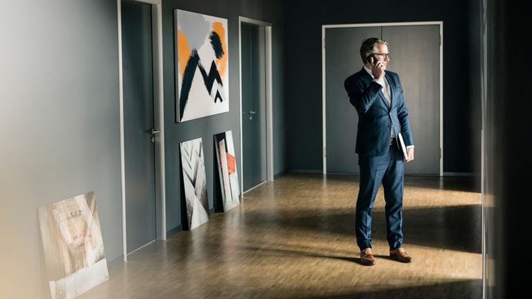 Business professional speaks on the phone in a gallery-like hallway, symbolizing AML risk in nonbank sectors like fine art and real estate.