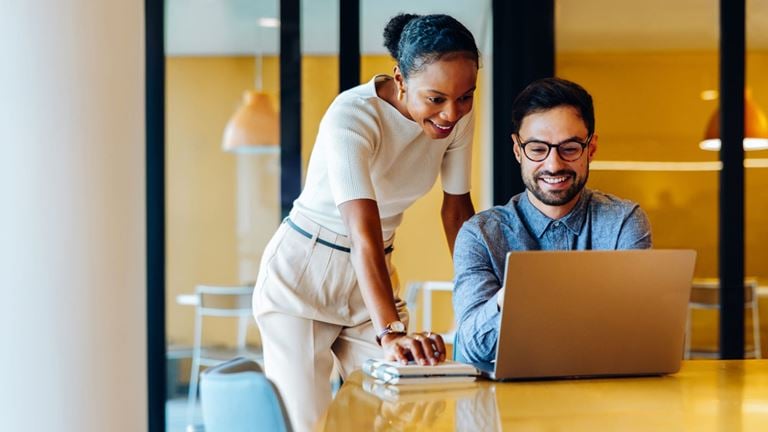 Two professionals collaborate on a laptop to address business challenges with AI.