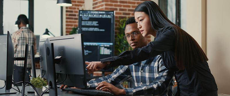 Two cybersecurity professionals review code at a workstation, representing cyber program maturity and tech-driven risk reduction.