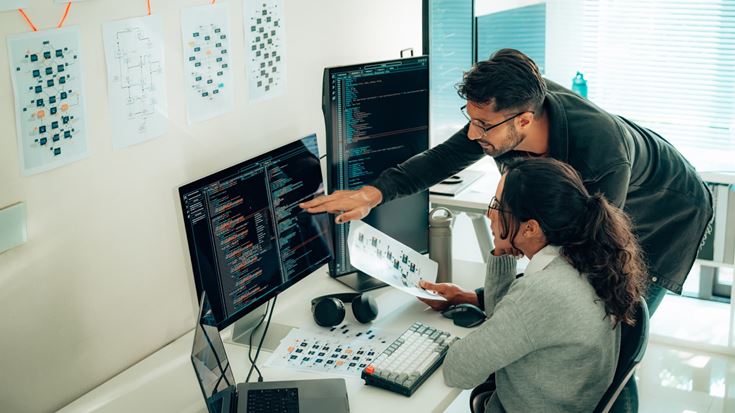 Two professionals analyze code on monitors, representing alignment of cybersecurity tools to protect infrastructure layers.