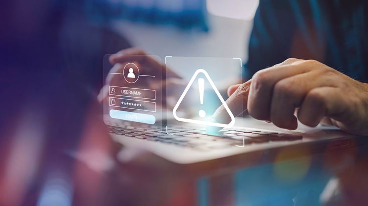 Hand on laptop with warning icon and login screen overlay, symbolizing AI-driven phishing and cyber risk mitigation strategies.
