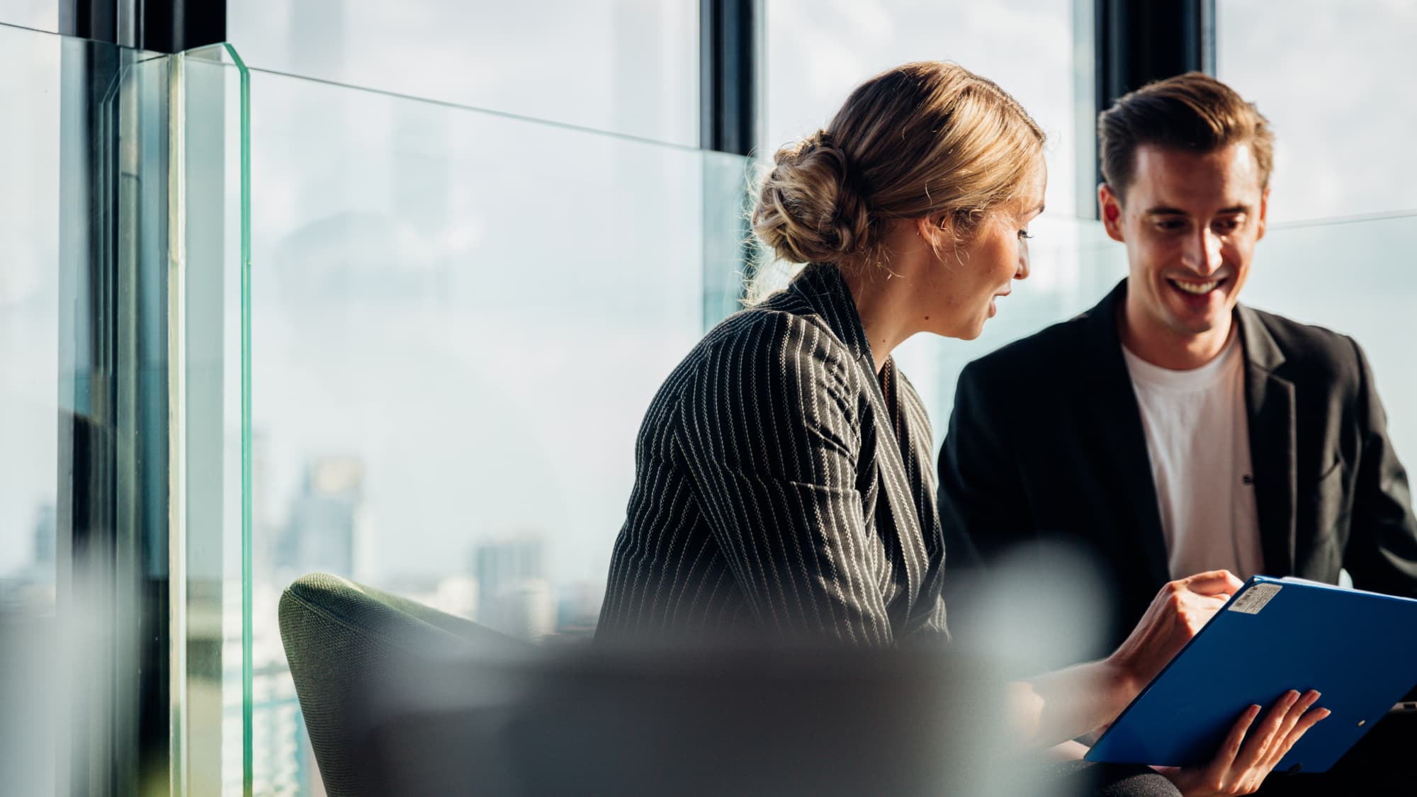 Two business professionals discuss customer onboarding while reviewing a tablet at a table, focusing on compliance insights.