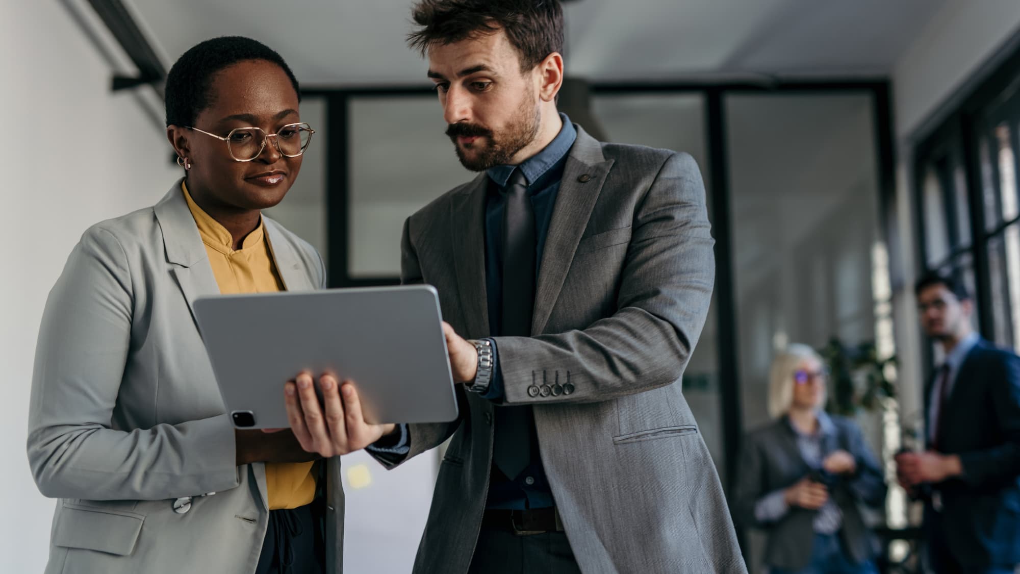 Two professionals review information on a tablet, illustrating collaborative AML advisory in financial services.