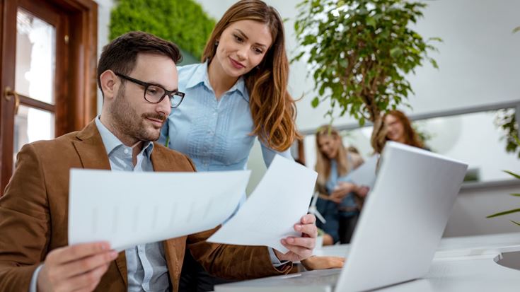 Two finance professionals review reports together at a laptop to improve financial visibility and reporting.