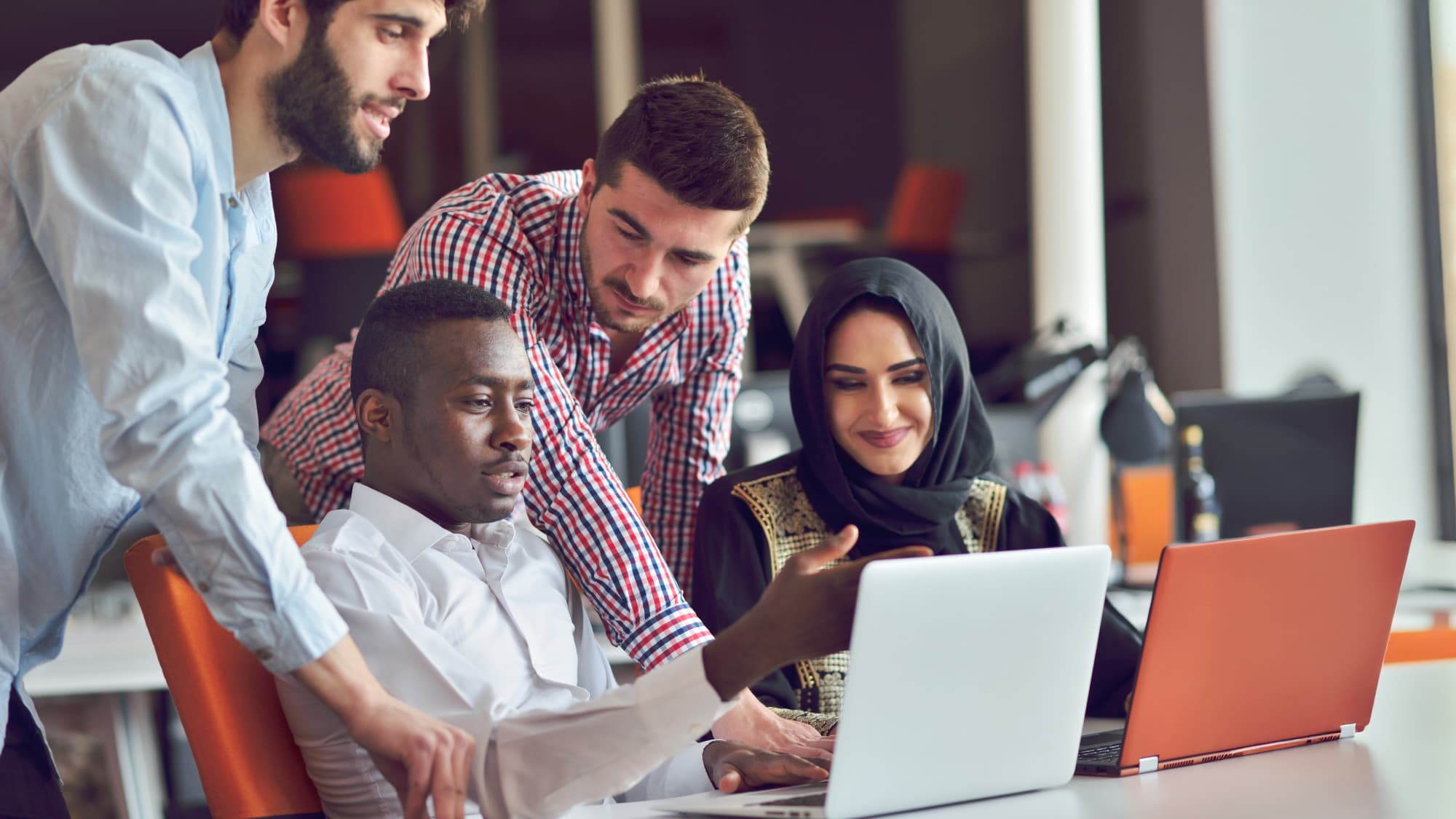 Diverse coworkers collaborating around laptops, reflecting teamwork and innovation in tech and operations.