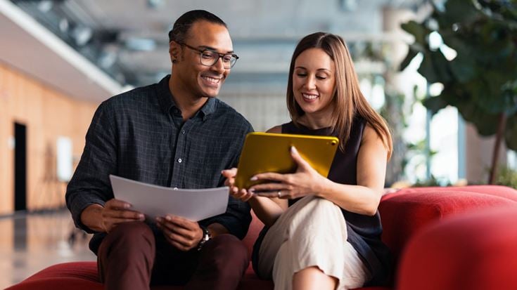 Two professionals review information on a tablet and document while discussing updates for state and local government financial reporting and compliance.