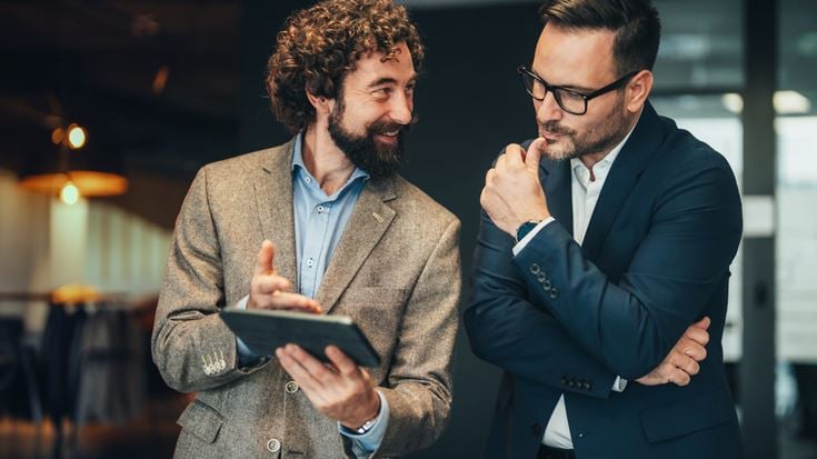 Investment advisers discuss compliance considerations while reviewing information on a tablet.