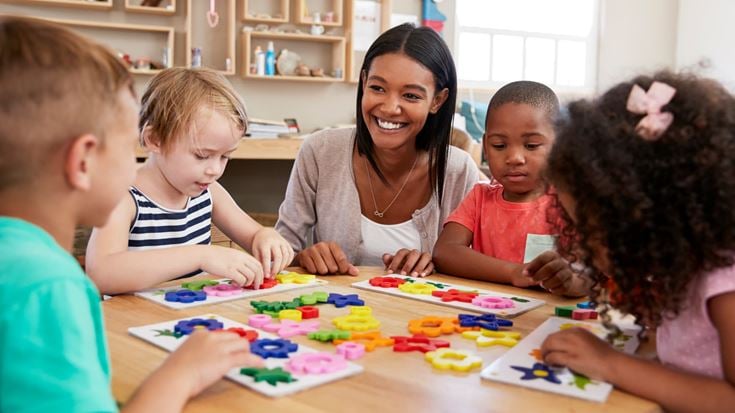 Teacher helps children with puzzles at a classroom table, representing support for exempt organizations and community services.