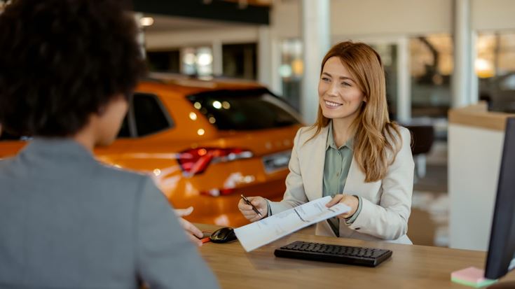 Car dealership employee reviews paperwork with a customer, illustrating vehicle financing and loan interest deduction eligibility.