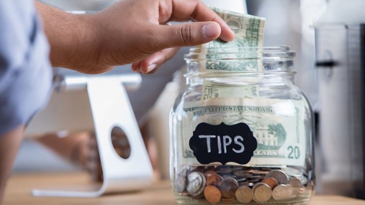 Cash tips placed in a jar, representing IRS regulations on reporting qualified tip income.