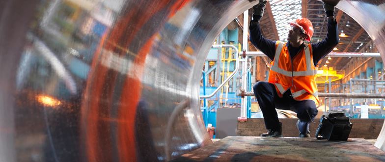 Metals worker inspects a large metal coil on the production floor.